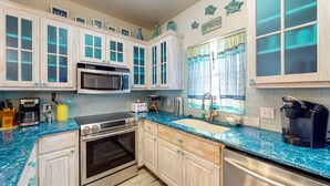 A modern kitchen with white cabinets, a built-in microwave, a stove, and a coffee maker.