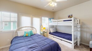 A bedroom with a bunk bed, a single bed with a headboard, a bedside table with a lamp, and a ceiling fan.