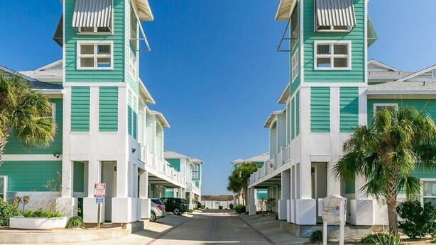 A row of two-story buildings with a flat roof, white and green exterior, and a clear sky.