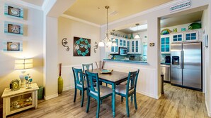A kitchen with a dining area, featuring teal chairs, a wooden table, and a stainless steel refrigerator.
