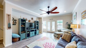 A spacious living room with a flat-screen TV, teal entertainment center, and a ceiling fan.
