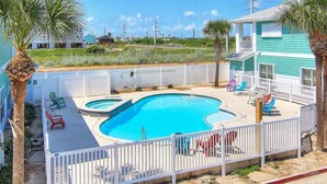 A swimming pool with a white fence, palm trees, and a blue house in the background.