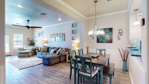A spacious living room with a large sectional sofa, a dining table with chairs, and a ceiling fan.