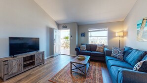 A living room with a TV, a sofa, a coffee table, and a view of the outside. - Room for Boat, Pet Friendly, Close to Community Pool (Port Aransas)