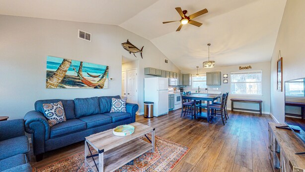 A spacious living room with a blue sofa, a wooden coffee table, and a colorful rug. A kitchen with a large island and modern appliances is visible in the background. - Room for Boat, Pet Friendly, Close to Community Pool (Port Aransas)