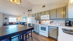 A modern kitchen with a dining area, featuring a large wooden table, white appliances, and green cabinets.