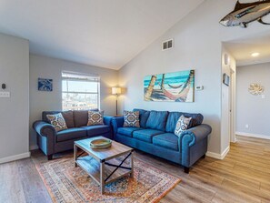 A living room with a blue sofa set, a coffee table, a patterned rug, and a painting of a beach scene.