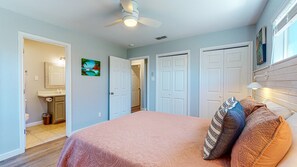 Une chambre à coucher avec un lit, un ventilateur de plafond et une porte donnant sur une salle de bain.