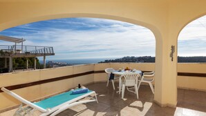 Un balcon avec un fauteuil de piscine, une table avec des chaises et une vue sur la ville et la mer.