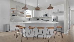 Een moderne keuken met witte kastjes, een centraal eiland met krukken, roestvrijstalen apparatuur en hanglampen.