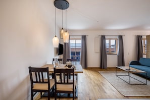 A modern living room with a dining area, a sofa, and a TV mounted on the wall.