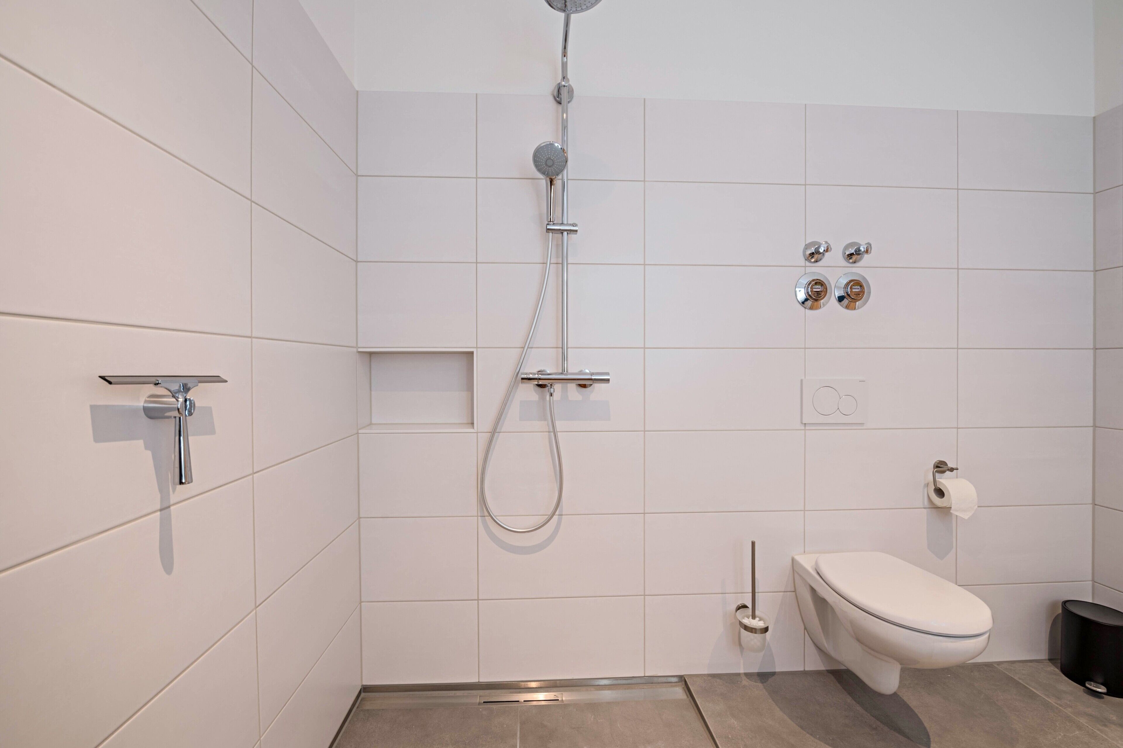 Een moderne badkamer met een douche, toilet en een handdoekhouder.