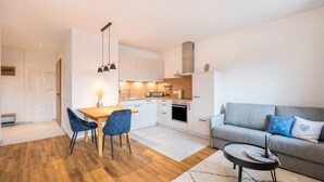 Una cocina moderna con armarios blancos, un comedor con mesa de madera y sillas azules, y un sofá gris con almohadas azules y blancas.