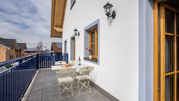 Ein Balkon mit Tisch und Stühlen, eine Holztür und ein blauer Geländer.
