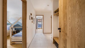 Ein Flur mit einer Holztür, einem Bett mit Bergmotiv und Blick auf einen Balkon.