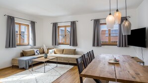 Ein modernes Wohnzimmer mit einer Couch, einem Esstisch und großen Fenstern.