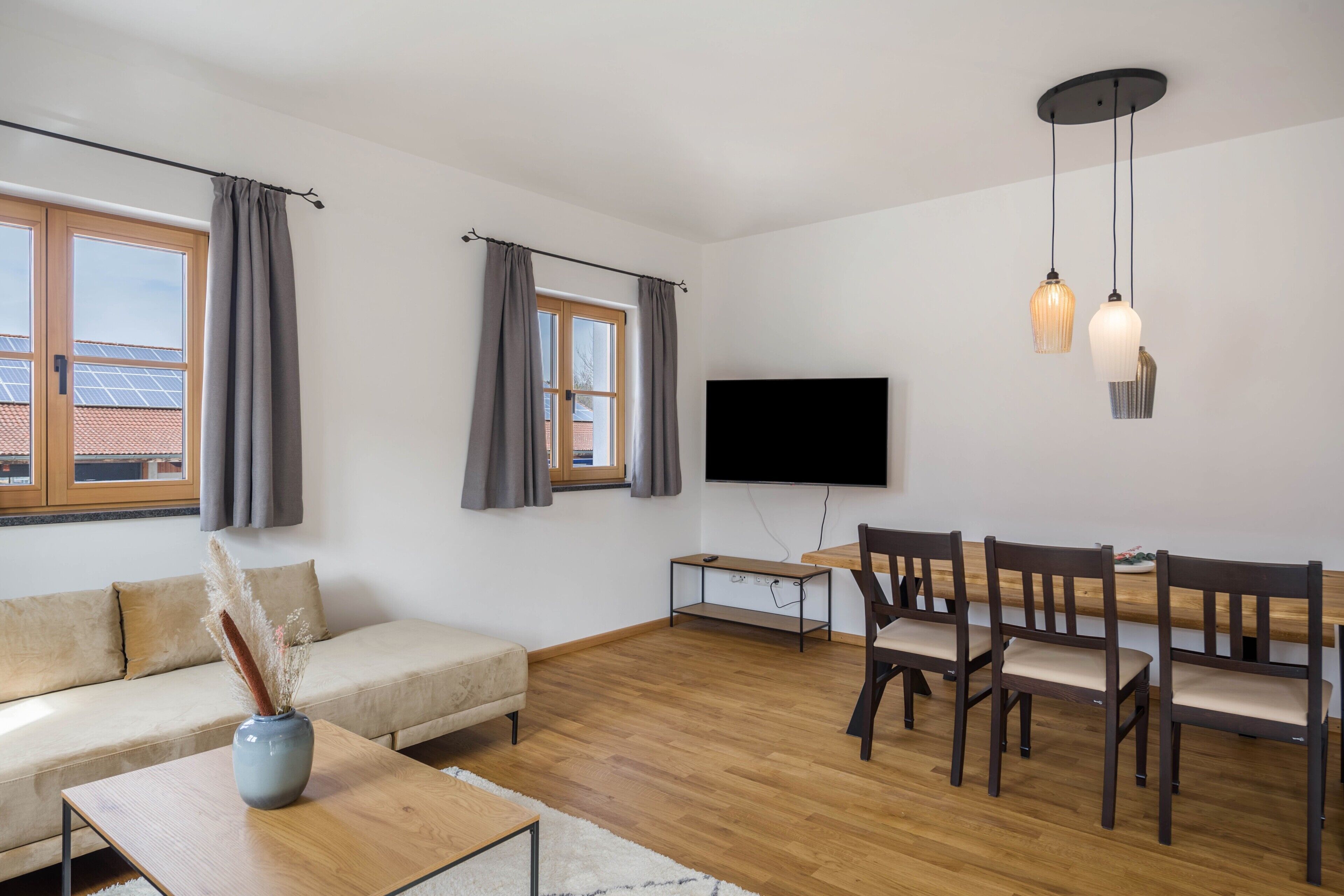 Una sala de estar moderna con sofá, mesa de comedor, sillas, televisor y ventana con cortinas.