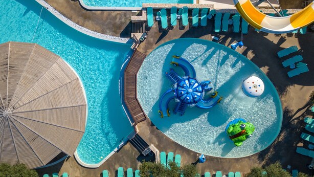 An aerial view of a resort with multiple swimming pools, a water slide, and sun loungers. - Iolida Village Hotel (Chania)