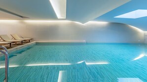 A modern indoor swimming pool with clear water, sunlit ceiling, and lounge chairs along the side. - Iolida Village Hotel (Chania)