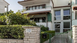 A two-story building with a stone wall entrance, a green gate, and a number '12' sign. - Cademia Two-bedroom Apartment 2 (Rovinj)