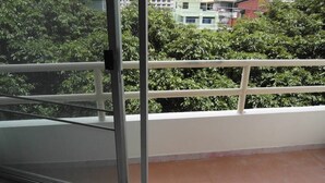Un balcón con puerta de cristal, piso de baldosas y vistas a zonas verdes y edificios.
