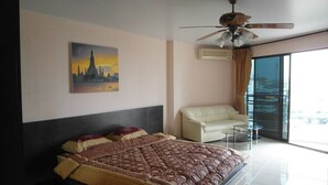 Una habitación de hotel moderna con una cama grande, un ventilador de techo, un cuadro de un paisaje urbano, un sofá y un balcón con barandilla de cristal.