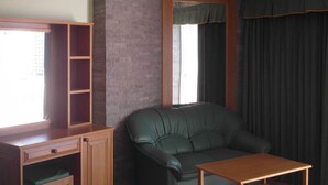 Quarto com sofá de couro verde, escrivaninha de madeira com prateleiras e janela com cortinas.