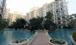 A multi-story residential building with a central swimming pool, surrounded by lush greenery and palm trees. - Plaza Residence F6 R62 Residence (Si Racha)