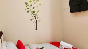 A hotel room with a bed, a wall-mounted TV, an air conditioner, and a wall decal of a tree. - Nice Double Room With Ac, Garden and Wifi (Bogor)