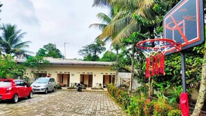A paved courtyard with a basketball hoop, parked cars, and a building with multiple doors. - Beautiful Deluxe Room With Ac and Wifi Well Located in Bogor (Bogor)