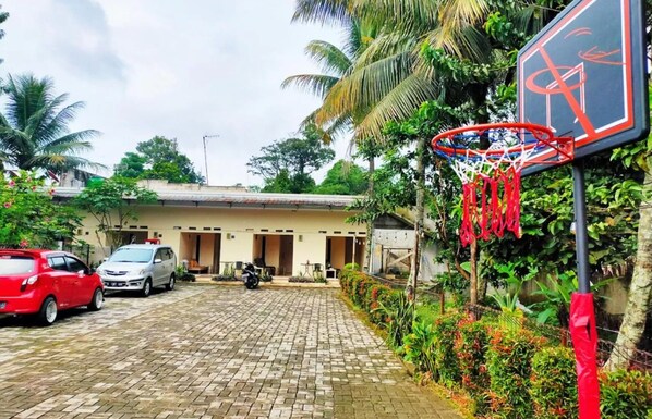 A paved courtyard with a basketball hoop, parked cars, and a building with multiple doors.