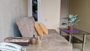 A living room with a sofa, cushions, a glass coffee table, a telephone, a decorative box, a small plant, and a wall-mounted light switch. - Beautiful Deluxe Room With Ac and Wifi Well Located in Bogor (Bogor)