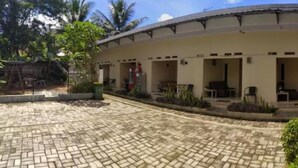 A building with a curved roof, multiple open doorways leading to rooms, and a paved courtyard. - Beautiful Deluxe Room With Ac and Wifi Well Located in Bogor (Bogor)