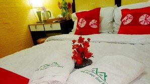A neatly made bed with white linens and red decorative pillows, a small red flower arrangement, and a set of white slippers with a logo. - Beautiful Deluxe Room With Ac and Wifi Well Located in Bogor (Bogor)
