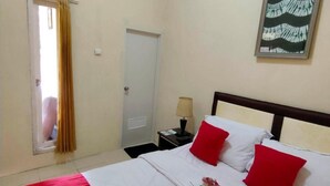 A hotel room with a bed, red and white bedding, a nightstand with a lamp, a framed picture on the wall, and a window with curtains. - Comfortable Room With Ac and Wifi for 2 People (Bogor)