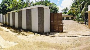 A long, narrow building with a series of windows along its length, adjacent to a paved area with a fence and trees in the background. - Beautiful Double Room With Ac and Wifi in Central Bogor (Bogor)