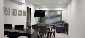 Uma sala de estar moderna com área de jantar, televisão de tela plana e arte decorativa nas paredes.