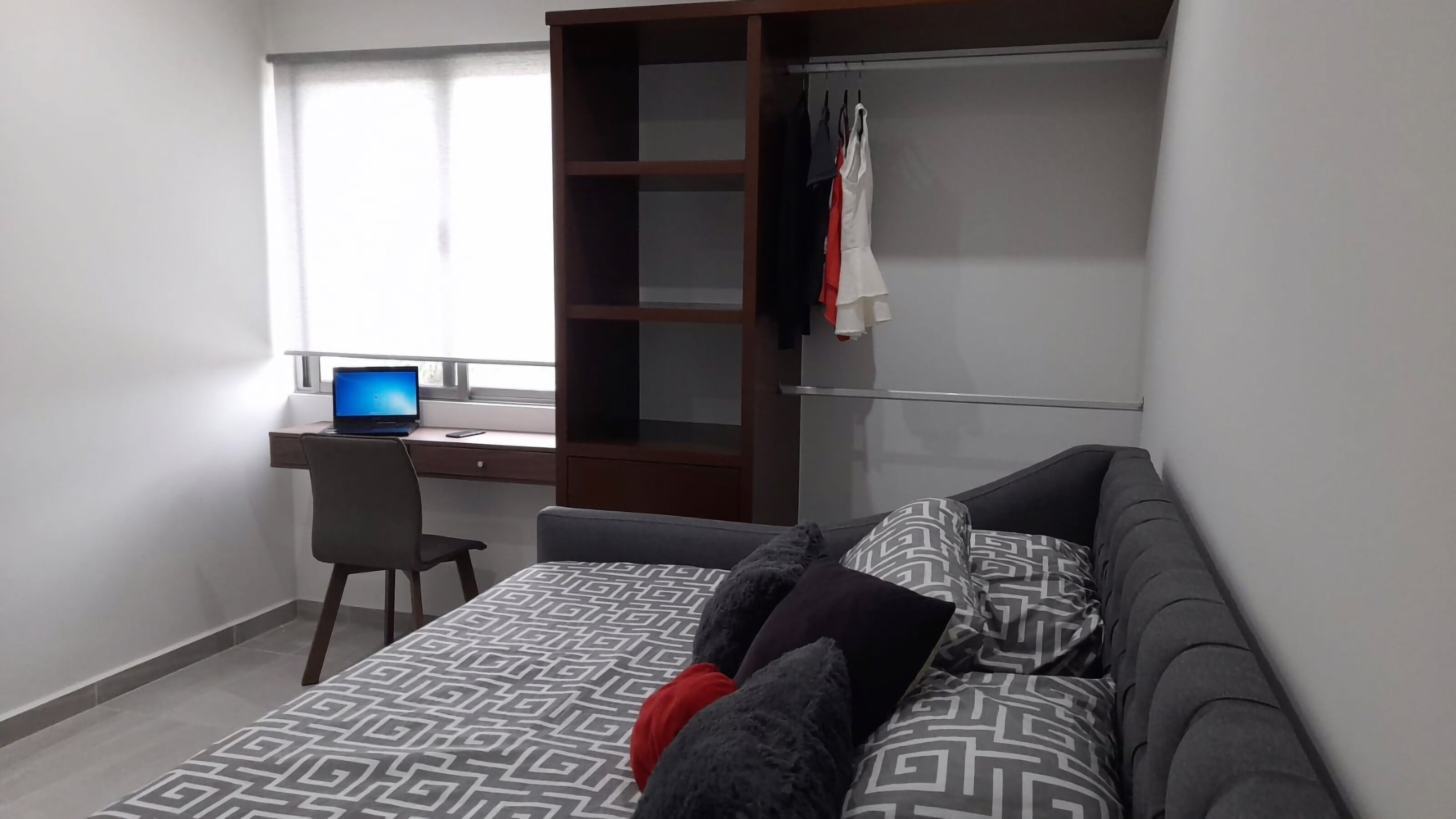 Une chambre à coucher avec un lit, un bureau avec un ordinateur portable, une chaise et une armoire.