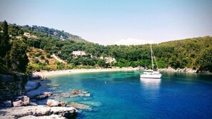 A coastal scene with a sailboat on clear blue waters, rocky shoreline, and buildings on a hillside. - Villa Elissavet - Kalami Bay - Family Pool House (Corfu)