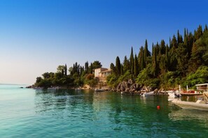A coastal scene with a house on a cliff, boats on the water, and dense trees. - Villa Elissavet - Kalami Bay - Family Pool House (Corfu)