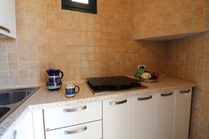 A kitchen with a sink, a stove, and a countertop with a blue mug and a bowl of vegetables.