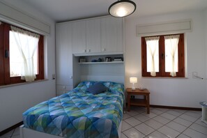 Una camera da letto con un letto, un comodino, uno scaffale con libri e una finestra con tende.
