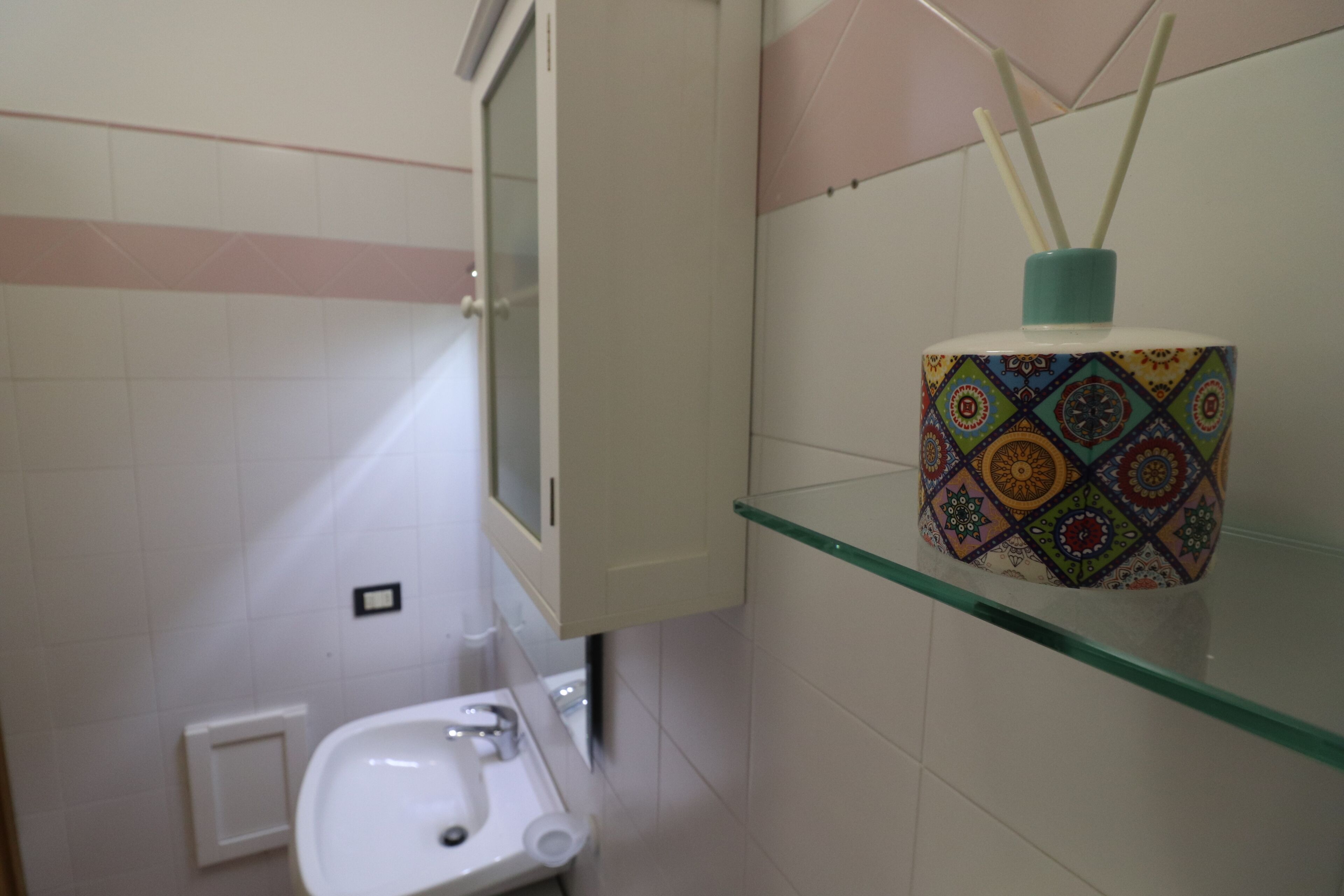 A bathroom with a white sink, a glass shelf with a decorative container, and a toilet.