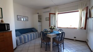 A compact living space with a kitchenette, a dining area with a table and chairs, a sofa, and a large window with curtains. - Casa Sophia Panoramic Terrace and Elegant Stay in the Heart of Otranto (Otranto)