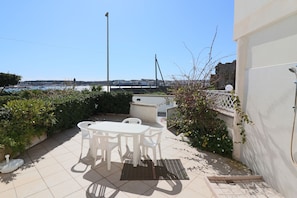 Un patio con un tavolo e sedie bianche, una fontana e vista sul mare e sugli edifici in lontananza.