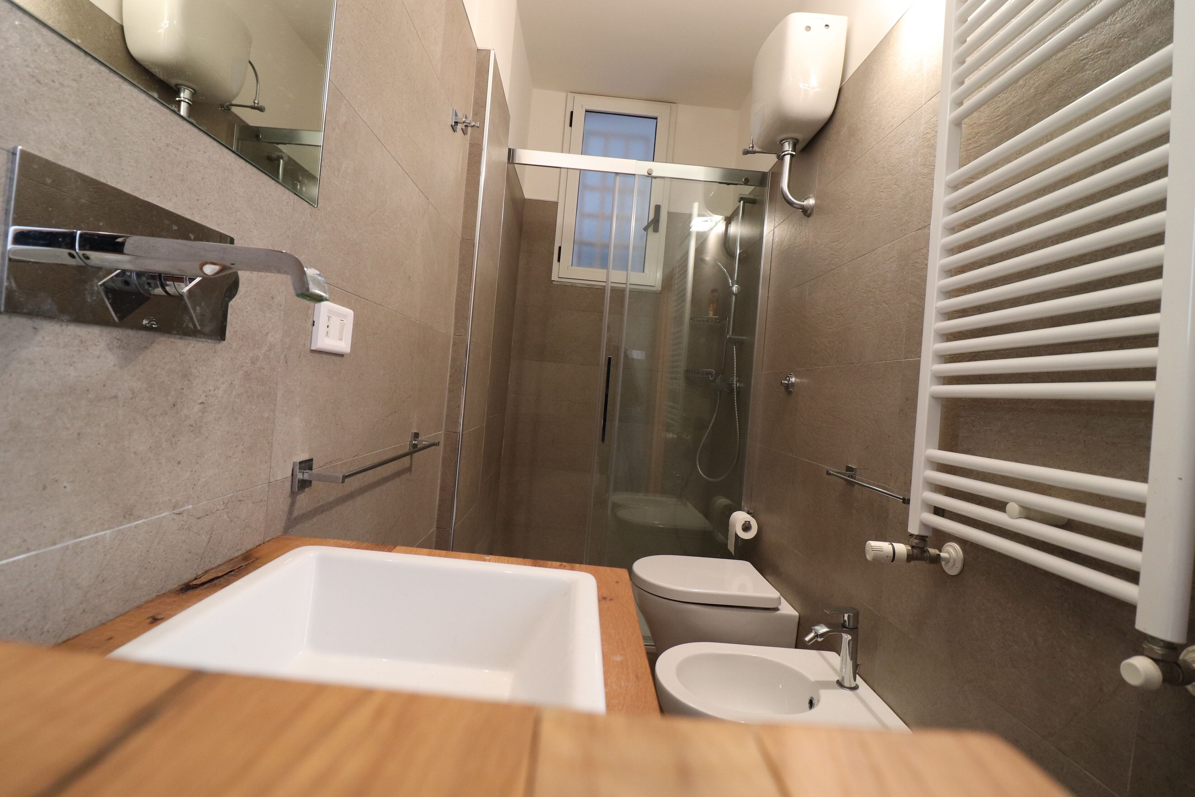 Une salle de bain moderne avec un meuble-lavabo en bois, un lavabo blanc, des toilettes et une douche à parois de verre.