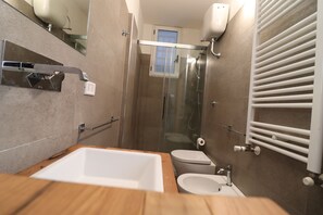 Un bagno moderno con un mobile bagno in legno, un lavandino bianco, un water e una cabina doccia in vetro.