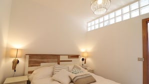 Ein Schlafzimmer mit einem hölzernen Kopfende, zwei Nachttischlampen und einem Fenster mit Jalousien.