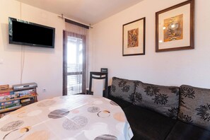 A room with a bed, a sofa, a TV mounted on the wall, and a window with curtains.