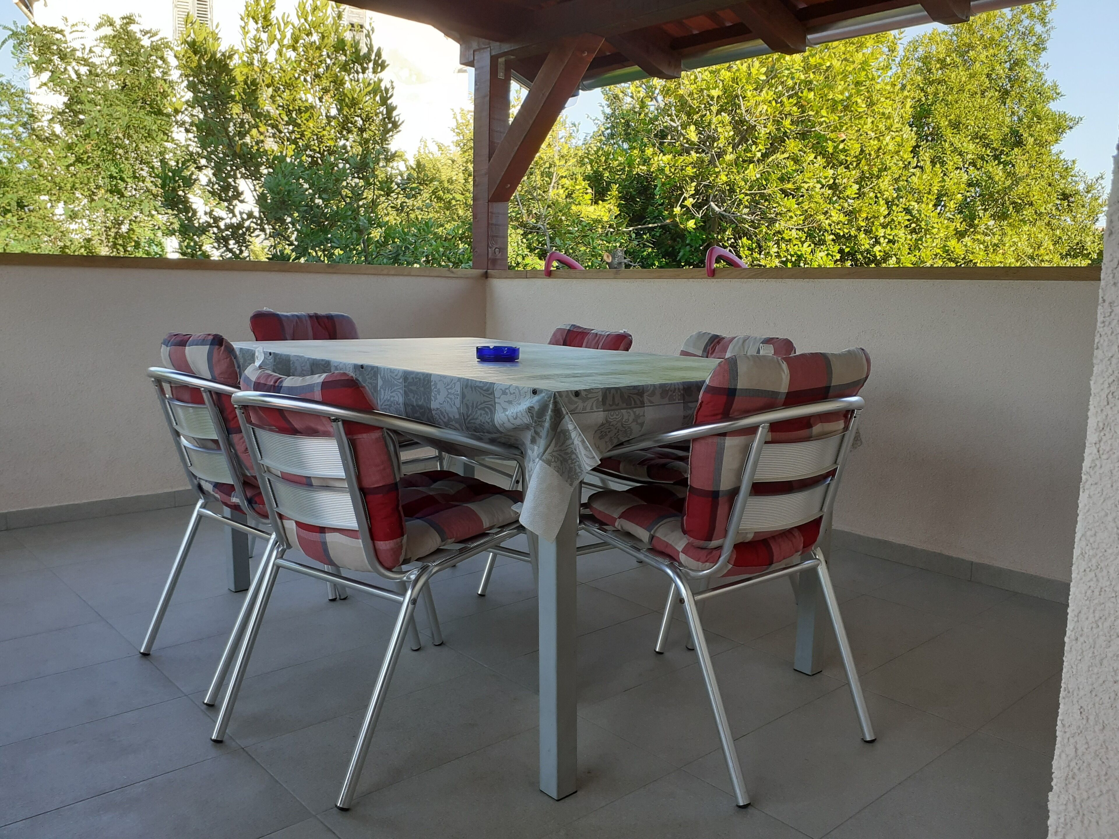 Un patio al aire libre cubierto con una mesa y sillas, rodeado de vegetación.